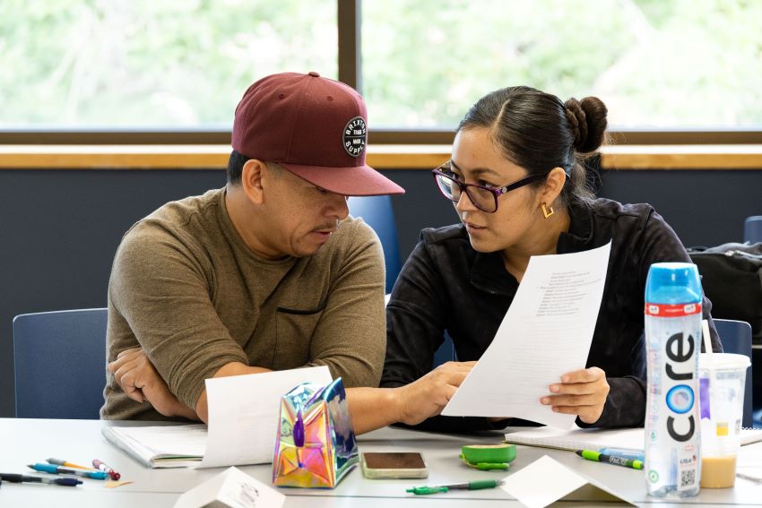 An adult student helps a man with an assignment at the Goodwill Excel Center.