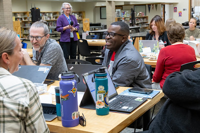 Educators at tables in the library, smiling and talking, instructor or facilitator standing in background