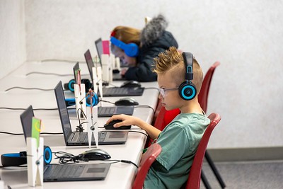 Students in a computer lab with laptops, focus is on male student with headphones and spiky hair concentrating