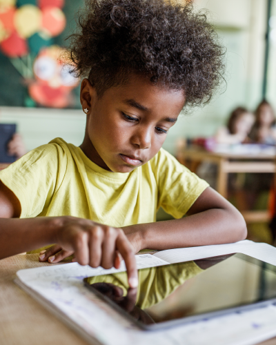 Young child using a tablet at a desk in a classroom setting