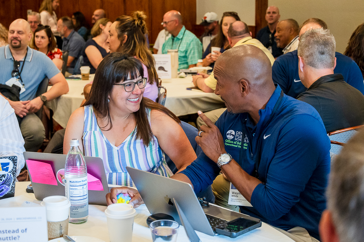 A woman and man talk at a table in a packed conference room. 