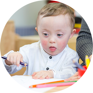 Young child with special needs using colored pencils in a classroom